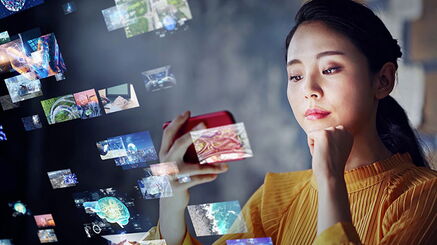Eine junge Frau blickt auf das Display ihres Smartphones, das sie im Querformat vor sich hält.