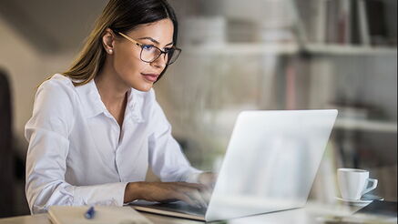 Eine Frau sitzt an einem Tisch, vor sich ein Notebook, auf dem sie tippt.